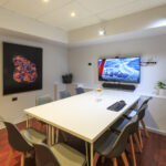 Well-lit meeting room with art on walls, seating and video conferencing set up