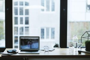 A laptop on a desk infront of a window looking out to another building