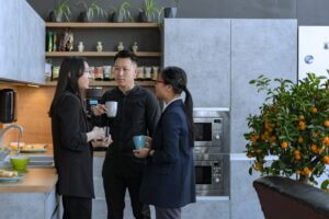 Three people in a kitchen chatting and holding coffee cups